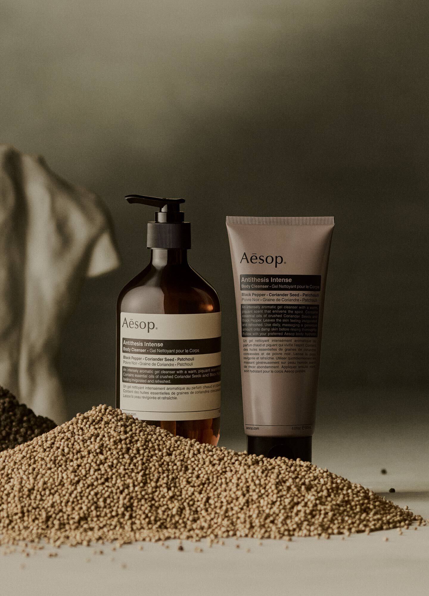 Aesop Antithesis Intense Body Cleanser pump bottle and tube beside piles of black peppercorns and coriander seeds.