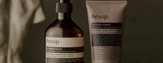 Aesop Antithesis Intense Body Cleanser pump bottle and tube beside piles of black peppercorns and coriander seeds.