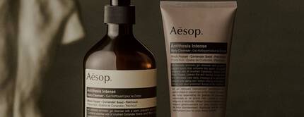 Aesop Antithesis Intense Body Cleanser pump bottle and tube beside piles of black peppercorns and coriander seeds.