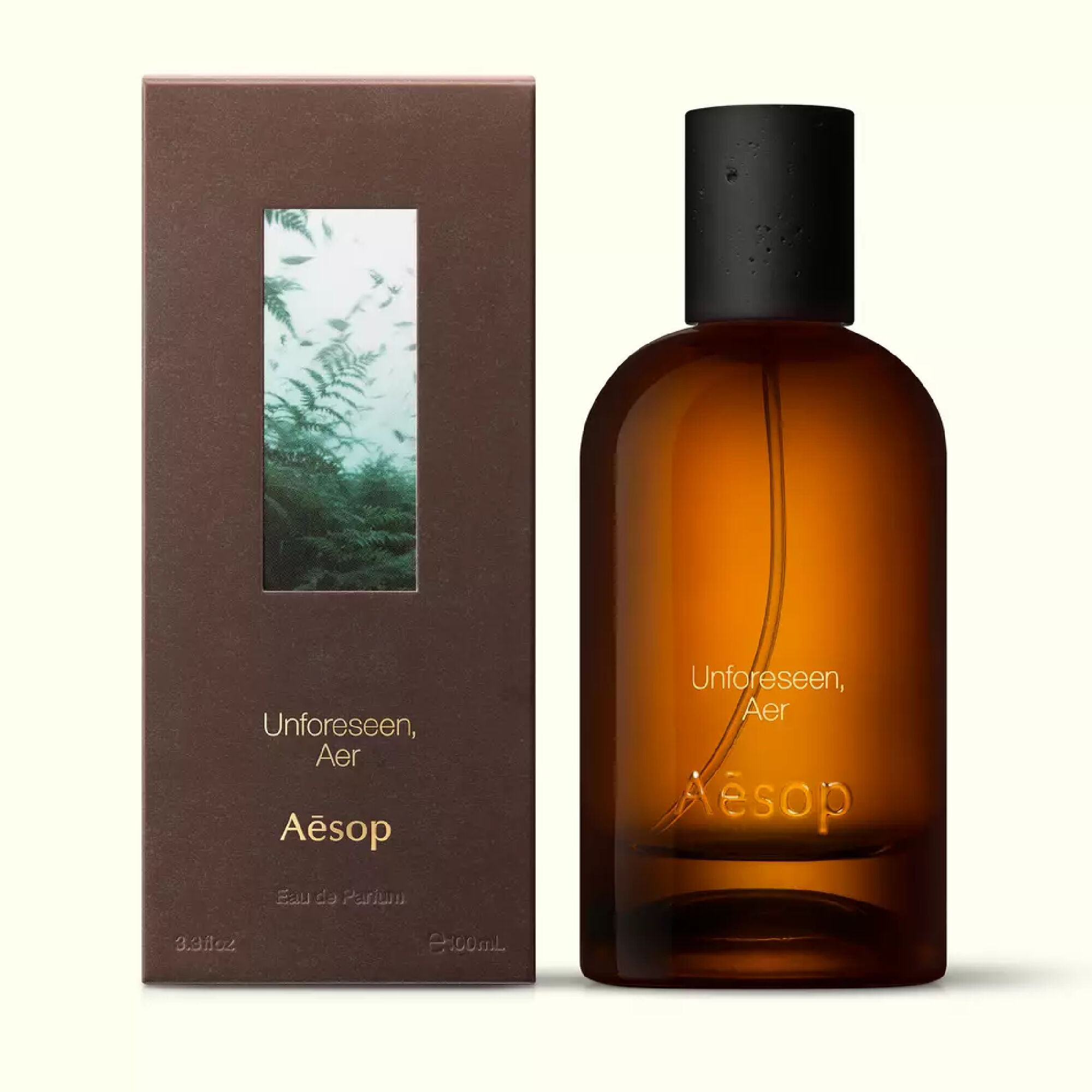 Amber glass Aesop Unforeseen Aer Eau de Parfum bottle beside its brown outer box on a white background.