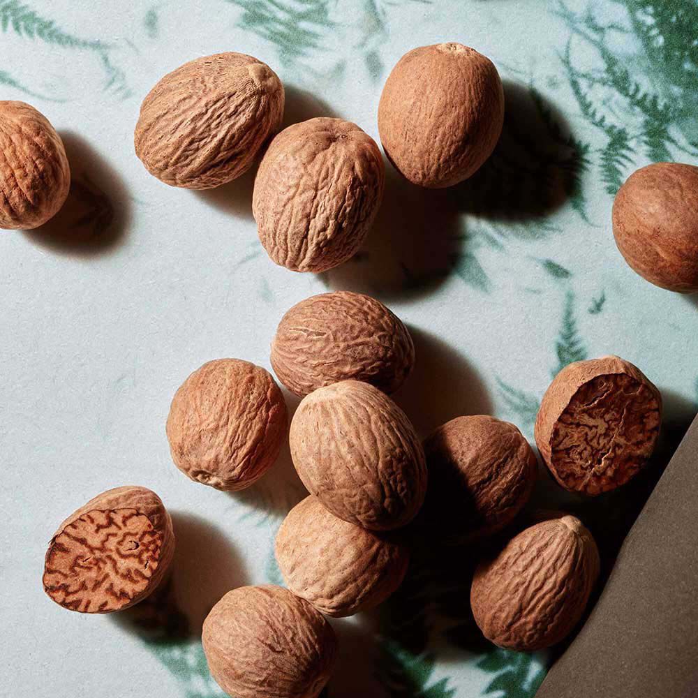 Scattered whole nutmegs on a dark surface.