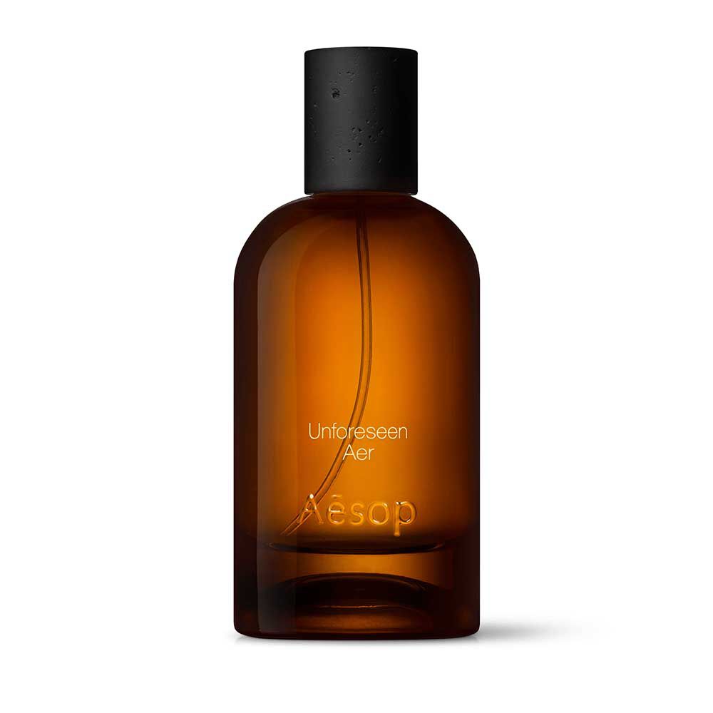 Amber glass Aesop Unforeseen Aer Eau de Parfum bottle with black cap on a white background.