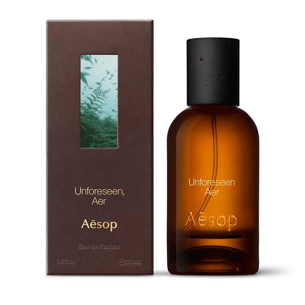 Amber glass Aesop Unforeseen Aer Eau de Parfum bottle beside its brown outer box on a white background.