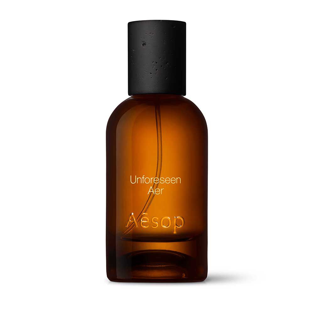 Amber glass Aesop Unforeseen Aer Eau de Parfum bottle with black cap on a white background.