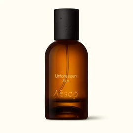 Amber glass Aesop Unforeseen Aer Eau de Parfum bottle with black cap on a white background.