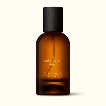Amber glass Aesop Unforeseen Aer Eau de Parfum bottle with black cap on a white background.